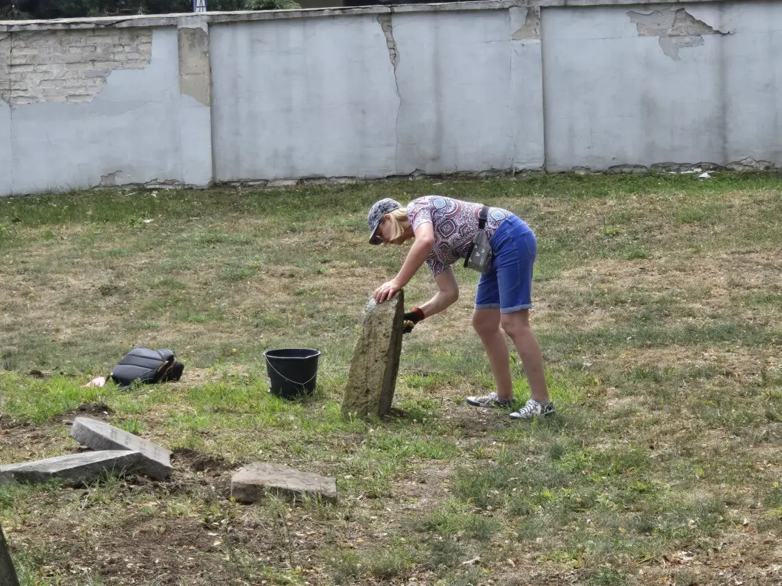 A woman in blue shorts and a hat is working on a tree stump.